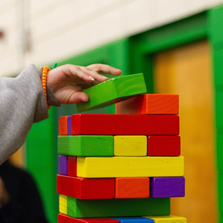 arm of child playing game of stacking colored blocks