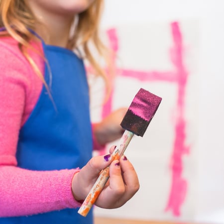 child holding foam paint brush that has pink paint on it