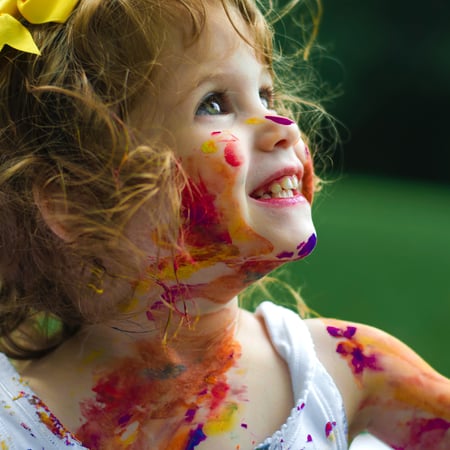 smiling child looking up with paint on face neck and arms